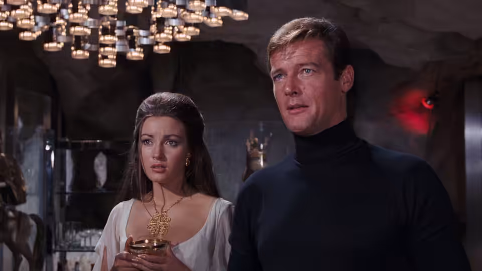 James Bond (Roger Moore) stands beside Solitaire (Jane Seymour) under chandeliers in a stone room