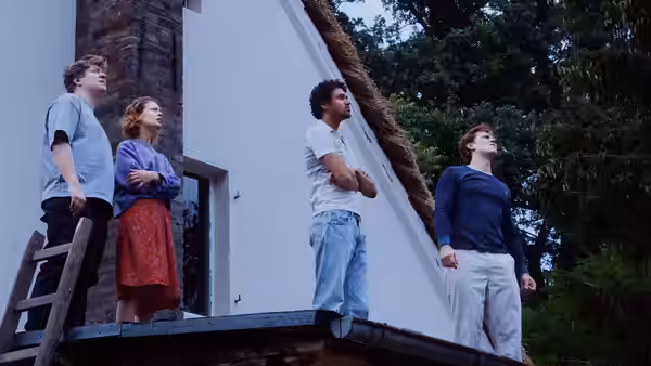 Four young adults stand on a rooftop looking up at the sky