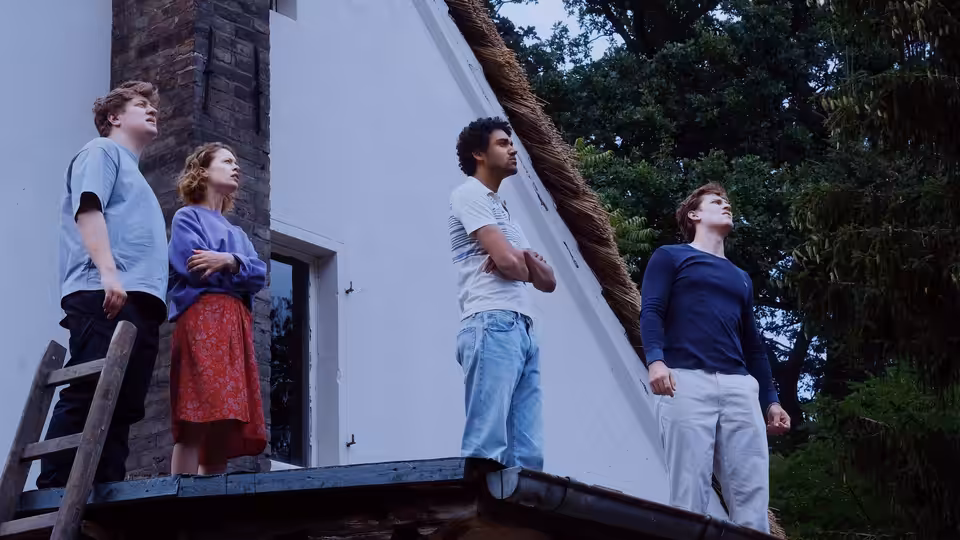 Four young adults stand on a rooftop looking up at the sky