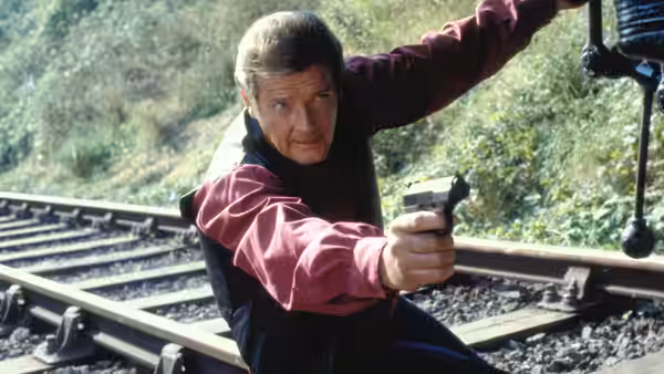 James Bond (Roger Moore) aiming a pistol while crouching beside railway tracks