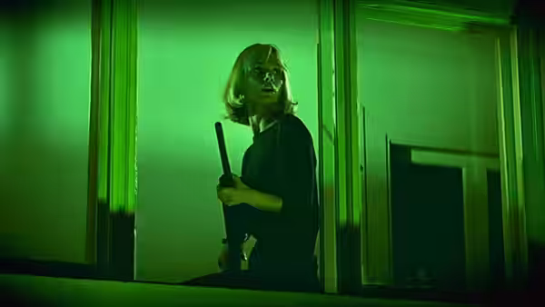 Kara Milovy (Maryam D'Abo) holding a long object in green-lit windows