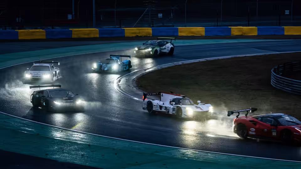 Race cars with headlights on navigating a wet track at night