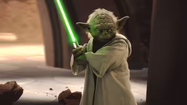 Yoda (Frank Oz) gripping a glowing green lightsaber in a fighting pose