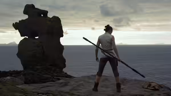 Rey (Daisy Ridley) stands on a rocky cliff by the sea holding a long staff