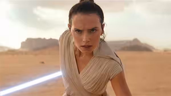 Rey (Daisy Ridley) gripping a lightsaber in a desert landscape