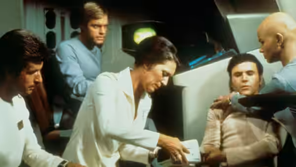 Uhura leans over a console while crew members attend to a seated man