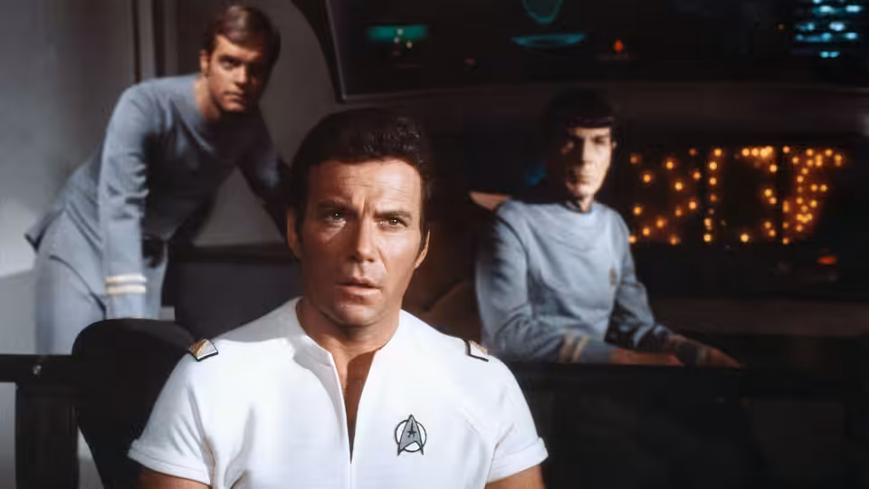 Admiral James T. Kirk seated on the bridge with Spock and another officer