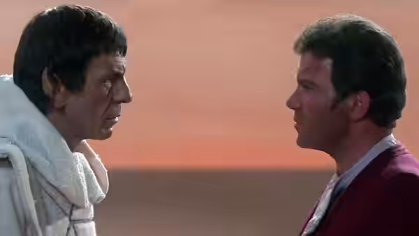 Two men facing each other closely against an orange sky