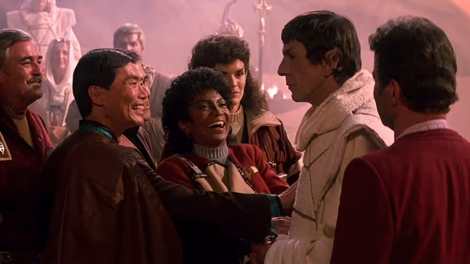 Starfleet officers gathered closely in a hazy reddish interior