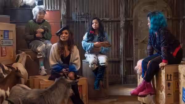 Women seated on crates inside a barn with goats nearby
