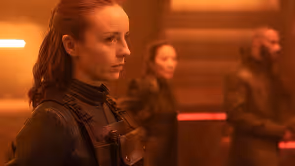 a red-haired woman in tactical gear standing in a dimly lit corridor