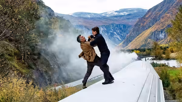two men grappling on a narrow ledge above a steep mountain valley