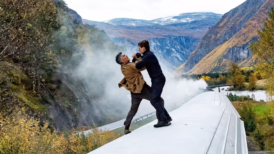 two men grappling on a narrow ledge above a steep mountain valley