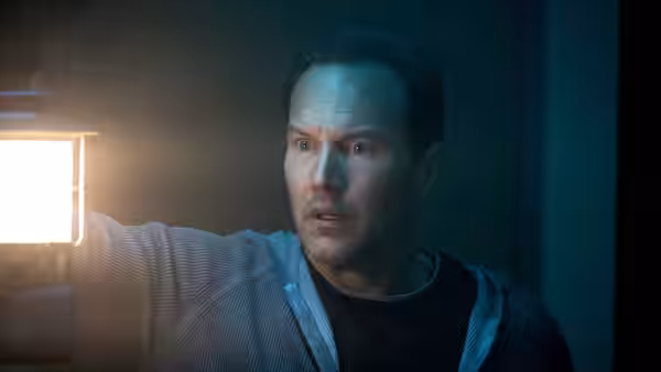 Josh Lambert (Patrick Wilson) holds a lantern while staring ahead with wide eyes