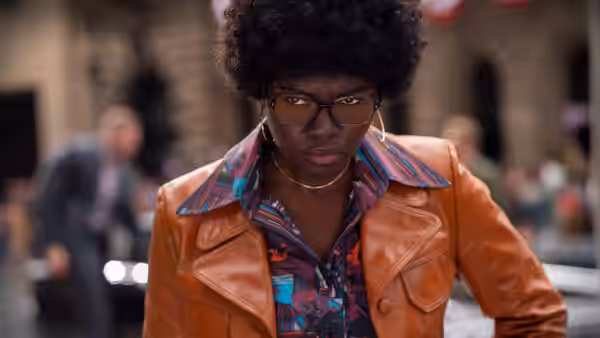a woman with afro hair and glasses wearing an orange leather jacket outdoors