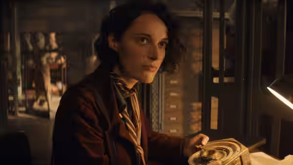 Helena (Phoebe Waller-Bridge) examining a circular artifact at a workbench