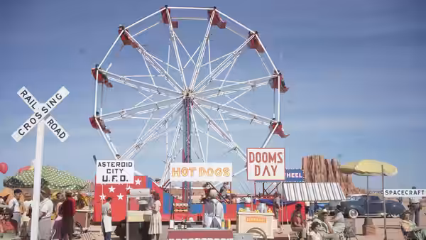 A Ferris wheel at a fairground with food stalls and signs