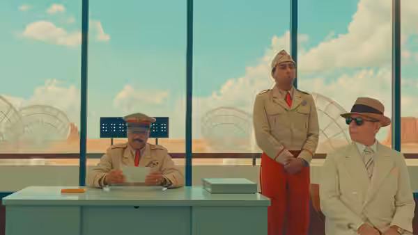 Three men in uniform and a suit seated at a desert office desk