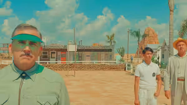 A man in a green visor standing in a desert town square