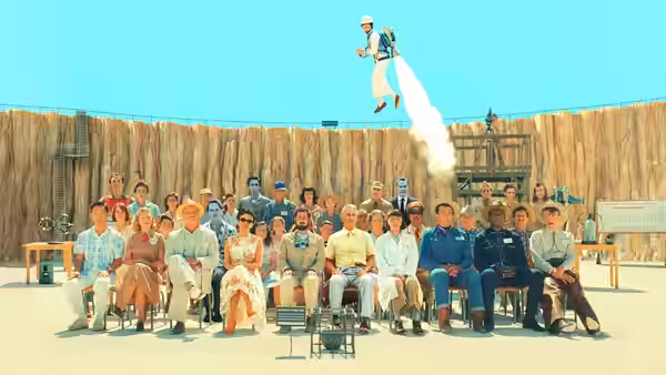 A crowd seated in an outdoor amphitheater watching a jetpack flight