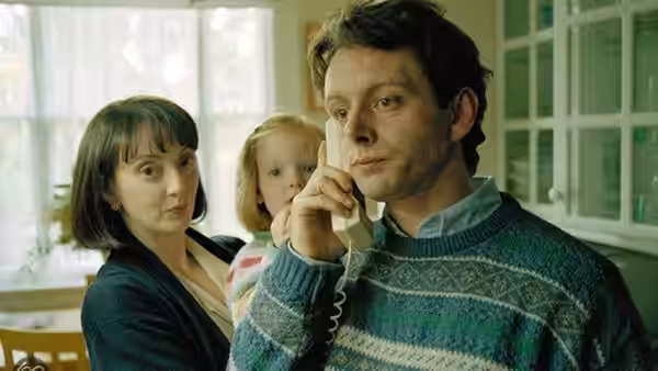 Gordon Brown (David Morrissey) talks on a telephone beside a woman and child