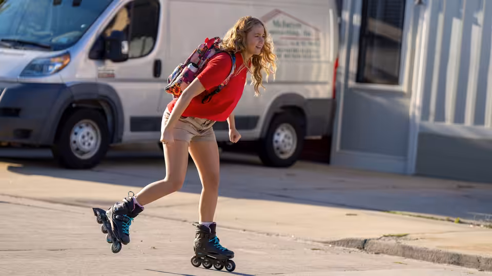 Maddie Barker (Jennifer Lawrence) rollerblading on a street beside a white van