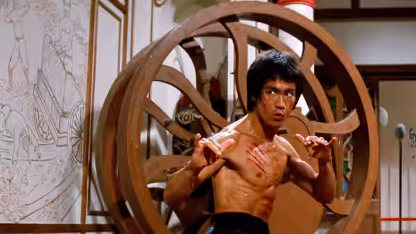 Lee (Bruce Lee) stands shirtless before a circular wooden partition, hands raised in a fighting stance