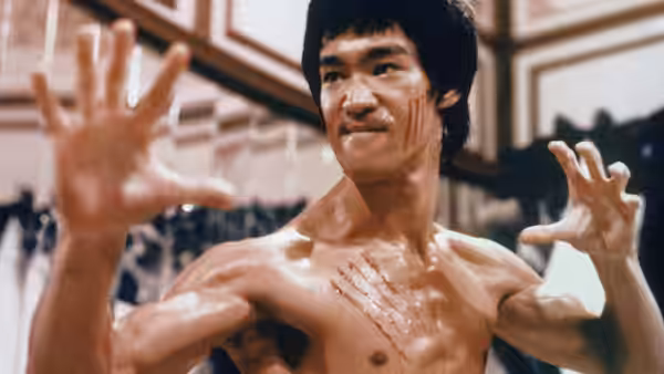 Lee (Bruce Lee) raises both hands in a martial arts stance inside the hall