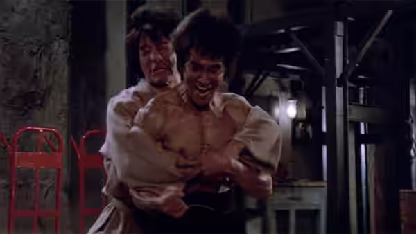 Williams (Jim Kelly) struggles as a man restrains him from behind in a workshop