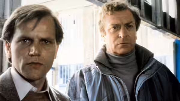 Valeri Petrofsky (Pierce Brosnan) stands beside John Preston (Michael Caine) near a doorway