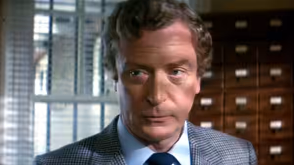 John Preston (Michael Caine) looks aside in an office lined with filing cabinets