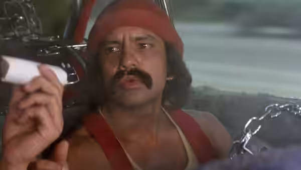 Man (Tommy Chong) sits inside the car, looking toward a hand holding a small paper
