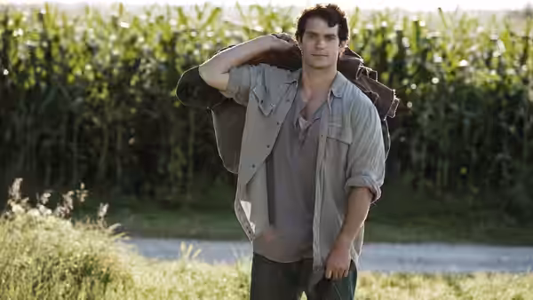Clark Kent (Henry Cavill) walks past a cornfield carrying a bag
