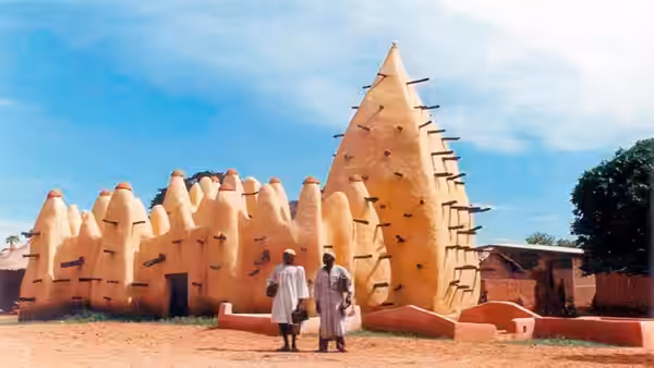 Two men stand before an earthen mosque and adjoining village buildings