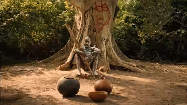 An elderly man sits beneath a marked tree beside three clay vessels