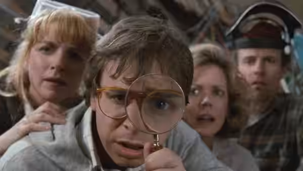Wayne Szalinski (Rick Moranis) examines something through a magnifying glass as three children watch