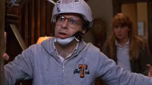 Wayne Szalinski (Rick Moranis) wears a makeshift helmet in his workshop as Diane looks on