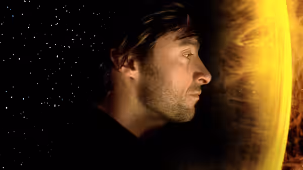 Tommy (Hugh Jackman) floats beside a glowing planet in a star-filled void