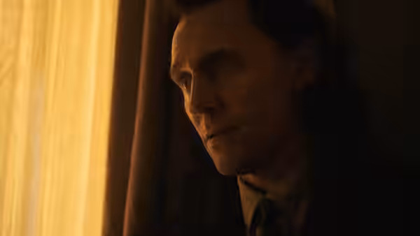Loki (Tom Hiddleston) looks past a glowing curtain in a dim room