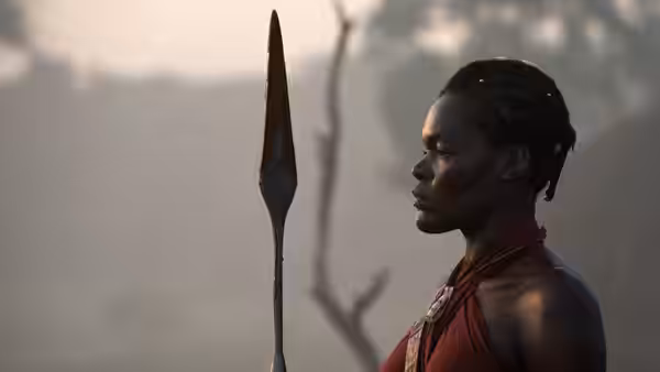 An Agojie warrior stands in profile beside an upright spear