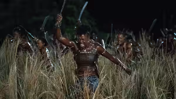 Nanisca (Viola Davis) raises her blade as Agojie warriors advance through tall grass