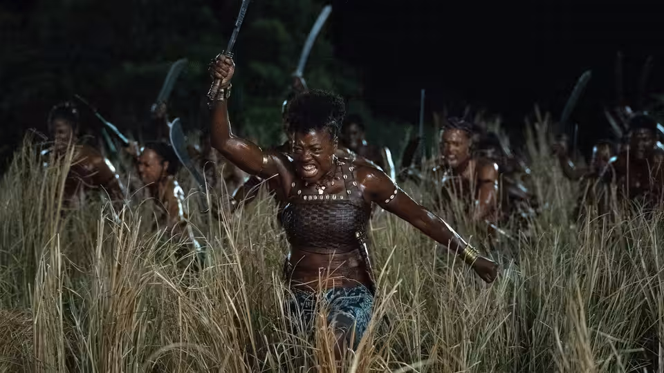 Nanisca (Viola Davis) raises her blade as Agojie warriors advance through tall grass