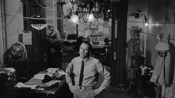 Bennett Marco (Frank Sinatra) stands with hands on hips in a cluttered office
