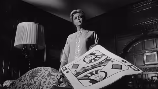 Raymond Shaw (Laurence Harvey) stands behind an elaborate mechanical device in a dark room