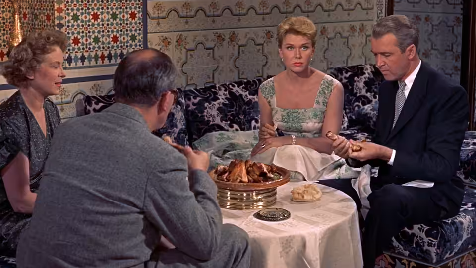 Jo McKenna (Doris Day) and Ben McKenna (James Stewart) sit at a restaurant table with other diners