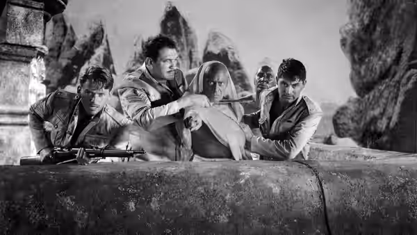 Several men gather around a veiled woman behind a low stone wall