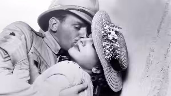 A uniformed soldier kisses a woman wearing a broad, flower-trimmed hat
