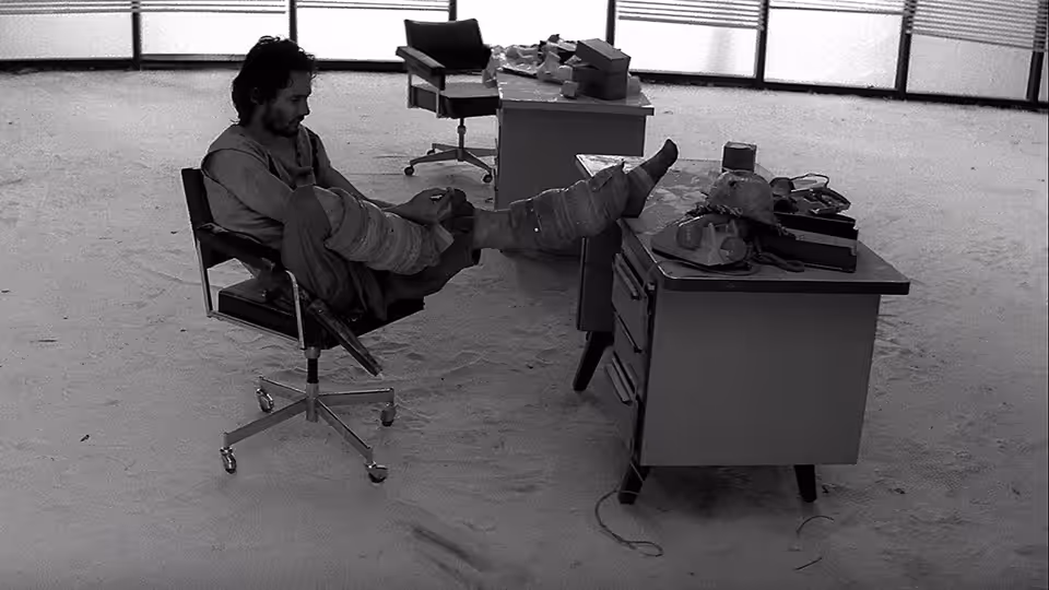 A man reclines with his feet on a desk in an empty office