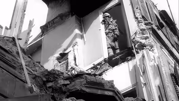 An armed man stands in a doorway amid the broken walls of a ruined building