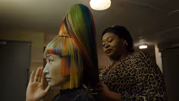 A stylist adjusting the colorful high ponytail of a seated client